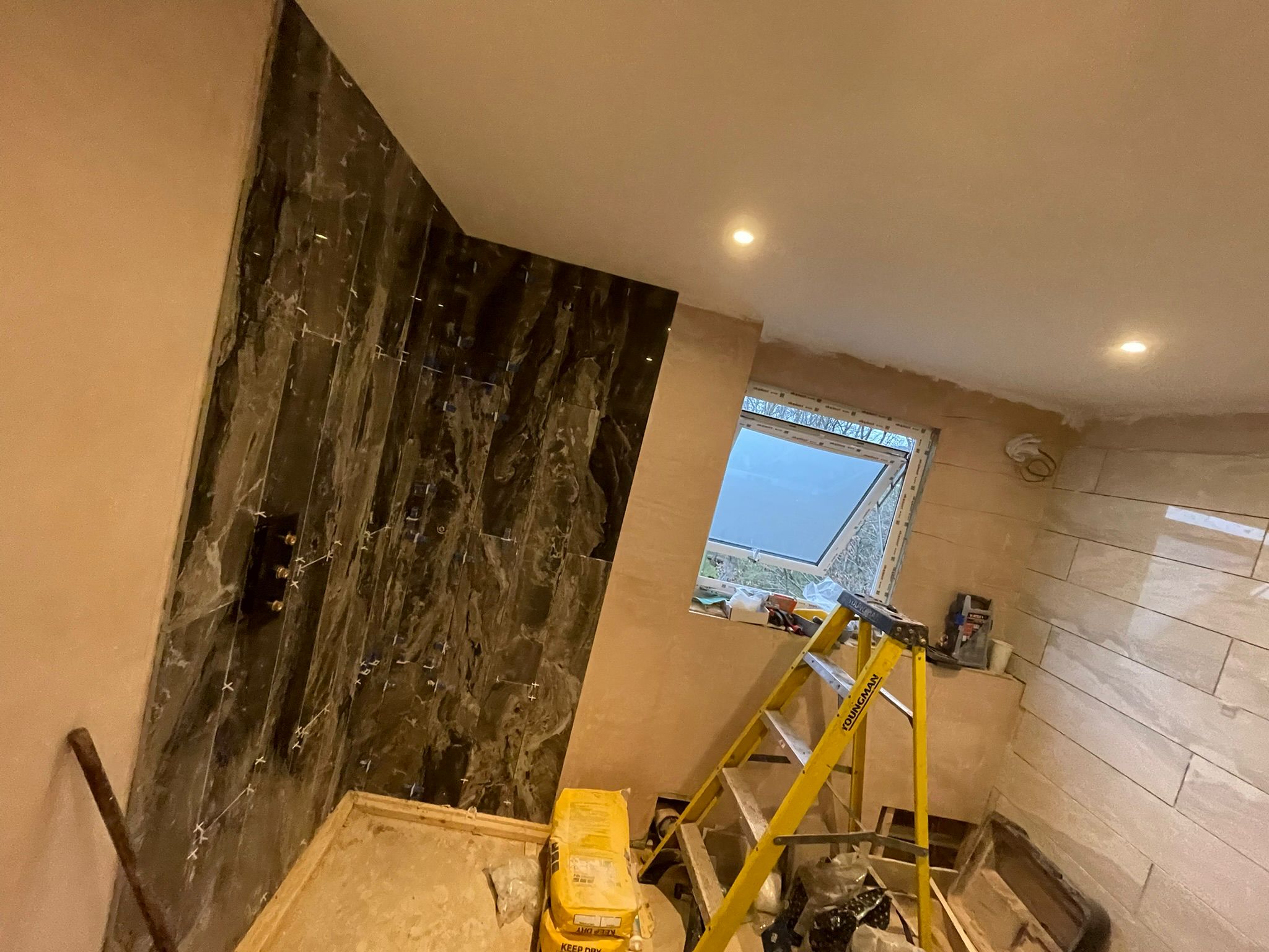 Dark marble shower wall tiling in progress